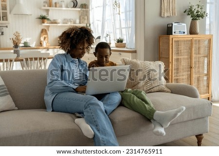 Happy african american family, mother and child looking at computer screen while talking video call. Mom and little son watching cartoons together on laptop while sitting on sofa at home