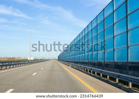 Road with noise reduction screen on the right. Driving on the highway near settlements. Royalty-Free Stock Photo #2314766439