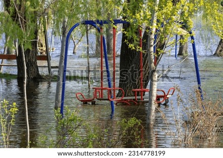Flood on bank river in spring time. Water filled play and sport grounds in city. Overflowed bank with sunken trees. Bottling shoreline flow and natural disaster. Climate change and ecological problem.