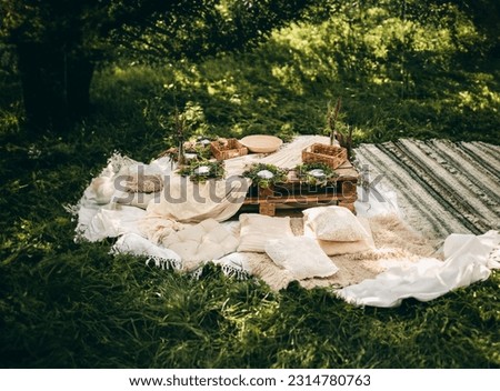 Beautiful white decor in boho style. Picnic in nature, table, carpets, pillows in the park. Celebration after quarantine.
