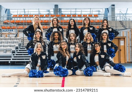 Smiling cheerleaders team posing for a picture with blue pompons on a court. High quality photo