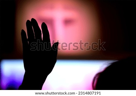 Silhouette hand raising, blurred christian cross background