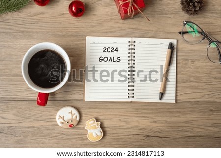 2024 GOAL with notebook, black coffee cup, Christmas cookies and pen on wood table. Xmas, Happy New Year, Resolution, To do list, Strategy and Plan concept