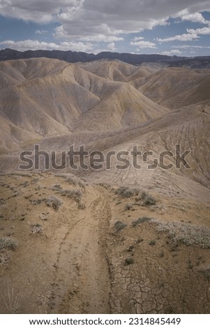 Portriat view of grey adobe clay badlands terrain in Peach Valley near Montrose Colorado with higher elevation mountains in background and dirt bike trails on ridge lines 