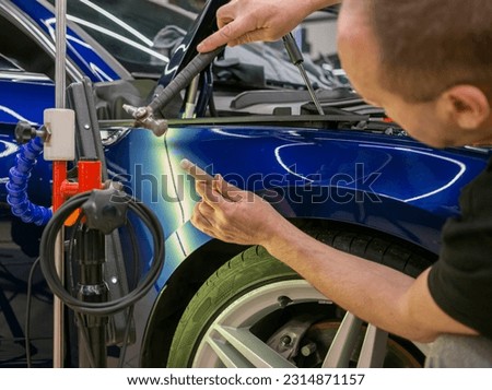 A specialist repairs a dent on the car body without painting. Process of paintless dent repair on car body. The mechanic at the auto shop with tools to repair dents in car body. Body repair. PDR.  Royalty-Free Stock Photo #2314871157