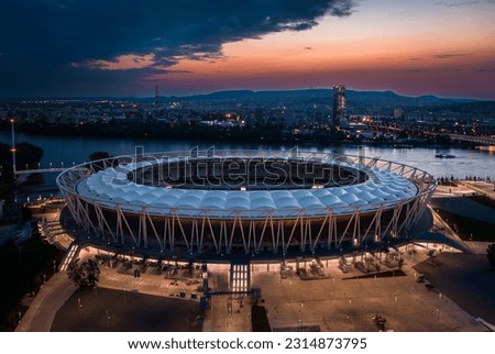 Budapest, Hungary - Aerial view of the illuminated National Athletics Centre at Danube riverbank with Rakoczi bridge, MOL Campus skyscraper building and colorful sunset sky at backgorund Royalty-Free Stock Photo #2314873795