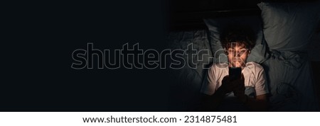 Young sleepy exhausted man lying in bed using smartphone at late night. Insomnia, sleep disorder concept. Addiction on a cell phone. Banner, copy space