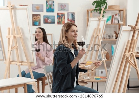 Women with glasses of wine attending painting class in studio. Creative hobby