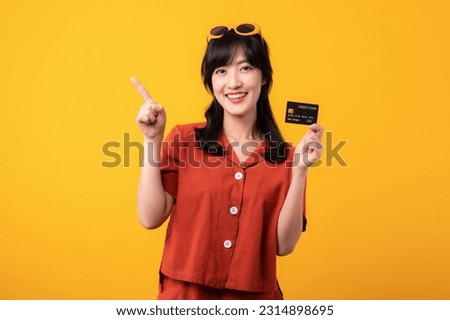 Portrait beautiful young asian woman happy smile dressed in orange clothes showing credit card and point finger to free space isolated on yellow background. Pay and purchase shopping payment concept.
