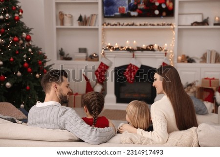 Happy family spending time on sofa near TV in cosy room, back view. Christmas atmosphere