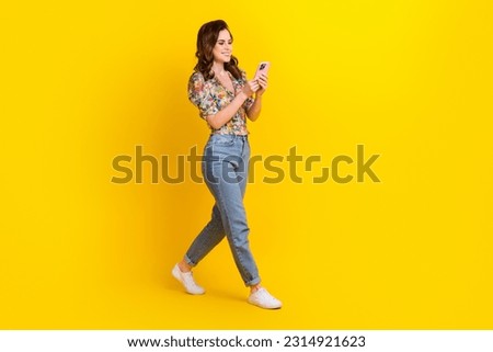 Full size photo of young brown hair girl wavy hair blouse flowers print chatting smartphone walking isolated on yellow color background
