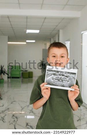A boy is standing in a dental clinic with a picture of his teeth in his hands. Portrait of a boy with an x-ray. Front view