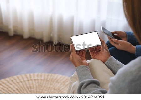 Mockup image of a couple woman holding and using a white mobile phone with blank desktop screen together