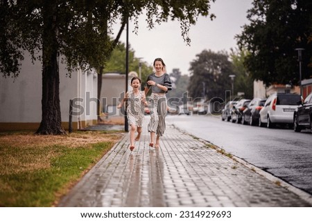 Young woman with coloured blond hair in grey t-shirt running on the street in the rain with little girl