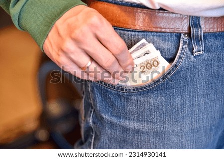 Man putting Polish money in the pocket of blue jeans. Banknotes of 100pln and 200pln.
