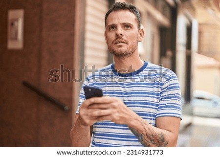 Young hispanic man using smartphone with serious expression at street
