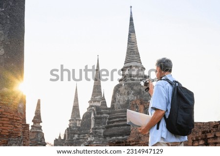 asian senior tourist male visit historic city,old man having a map,backpack,camera,is taking photo at Ayutthaya historical temple in evening sun,elderly people lifestyle,travel in archaeological site