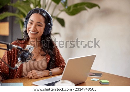 Smiling mixed race woman recording podcast in studio while looking away. Confident latin woman with headphones, microphone and laptop recording a podcast at home studio with copy space.