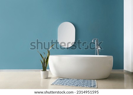 Simple interior of bathroom with bathtub, mirror and houseplant near blue wall Royalty-Free Stock Photo #2314951595