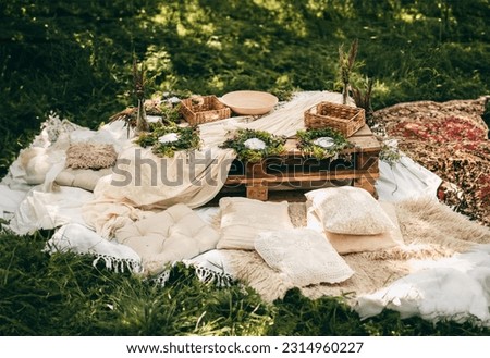 Beautiful white decor in boho style. Picnic in nature, table, carpets, pillows in the park. Celebration after quarantine.