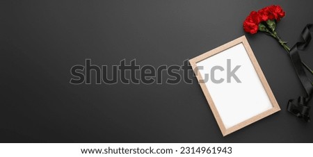 Blank photo frame, black funeral ribbon and carnation flowers on dark background with space for text