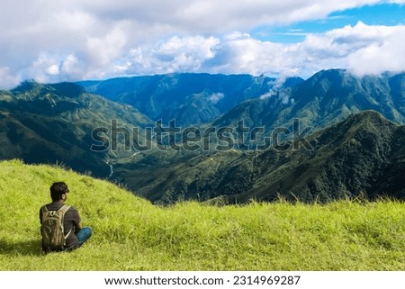 A man sitting on a grassy hill overlooking a valley