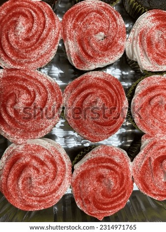 The top down view of a tray of cupcakes with vanilla frosting and red sprinkles.