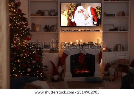 TV set with Christmas movie above fireplace in cosy room. Winter holidays atmosphere