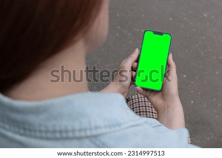 A woman holds a smartphone with a blank screen to replace it with a text message or informational content. Empty phone space to copy promotional content. Phone in hand in an urban environment