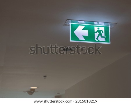 Green Emergency Exit Sign Illuminated on the Ceiling Corridor of an Apartment Building. Left Arrow for Directions in the Event of Fire. Way Out Sign. 