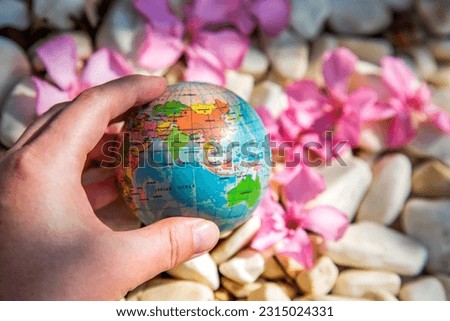earth in hand against white stones and pink flowers nature background. Ecology and environment concept