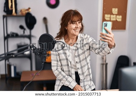 Middle age woman musician smiling confident make selfie by smartphone at music studio