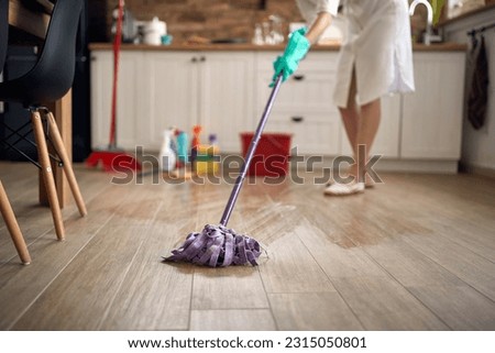 Faceless shot of houswife moping floor in the kitchen, with chemical bottles in the background. Home, cleaning, lifestyle concept. Royalty-Free Stock Photo #2315050801
