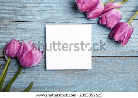 Card mockup, white blank wedding invitation with floral decor on bue wooden background. Square greeting card mockup with purple fresh flowers on table