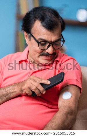 vertical shot of Elderly senior man checking glucose level by tapping smartphone to monitoring sensor at home - concept of health care, technology and mdicare. Royalty-Free Stock Photo #2315055315