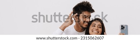 East asian young man and woman smiling and taking selfie photo with cellphone isolated over white background
