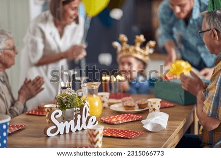 Blurred image of happy family celebrating little girls birthday together, sitting by kitchen table together singing and cheering. Home, family, celebration concept.