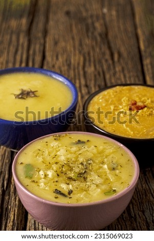 Three delicious hot broths from Brazilian cuisine, cassava, onion and Quenga, served in colorful porcelain pots, with a view from above on a beautiful rustic wooden table typical of a farm