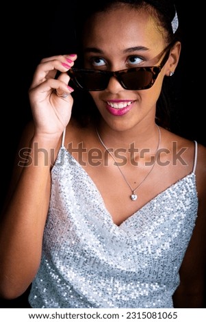 Beautiful teen girl posing for photo in studio. Wearing sunglasses. Isolated on black background.