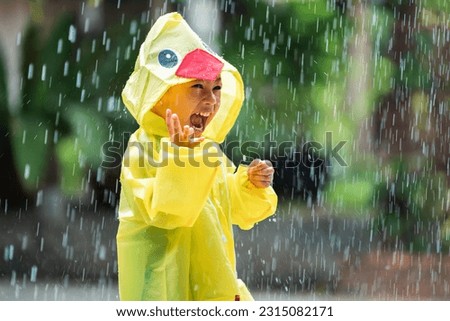 Asian boy wearing a raincoat outside the house. He is playing in the rain. Royalty-Free Stock Photo #2315082171