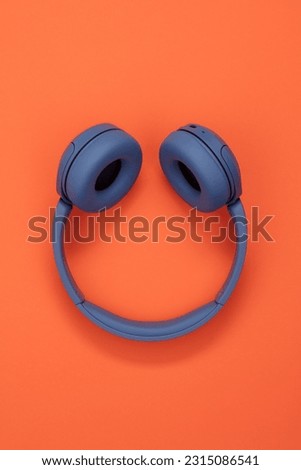 Blue headphones on orange background. Wireless headphones.  Headphones in the shape of a smile. 