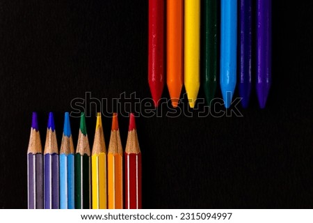 Crayon and pencil colors in antiparallel arrangement placed over black background.