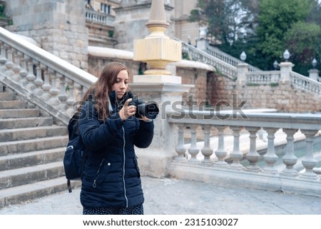 Concentrated woman Latin female photographer in warm clothes taking photos of National Art Museum of Catalonia on camera while walking in Barcelona, Spain