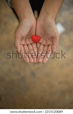 A small red heart symbolizes the love, kindness and friendship that a young woman offers to someone. Concept of using hearts as a symbol of love, friendship, kindness and compassion. Royalty-Free Stock Photo #2315120089