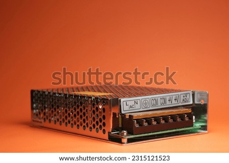 Switching power supply to convert AC current to DC. SMPS or Switched-Mode Power Supply with chrome metal case on orange background isolated. Royalty-Free Stock Photo #2315121523