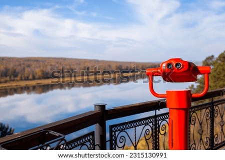 Public stationary binoculars on the banks of the river in summer or autumn to look at nature, coin-operated red metal binoculars. Royalty-Free Stock Photo #2315130991