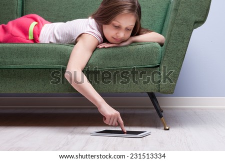 little girl using a tablet relaxed on a green sofa