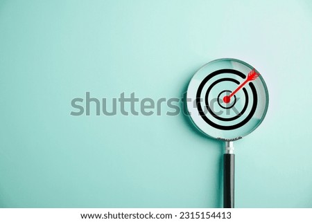 In this stock photo, a target board is magnified through a glass lens, symbolizing the business objective, target search concept, and achieving success. Isolated on a background with copy space.