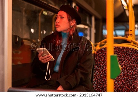 Teen asian woman in black hat messaging on smartphone at the bus