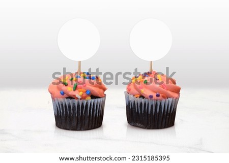 Closeup of two feisty pink frosted chocolate cupcakes resting in a classy minimalist kitchen scene.